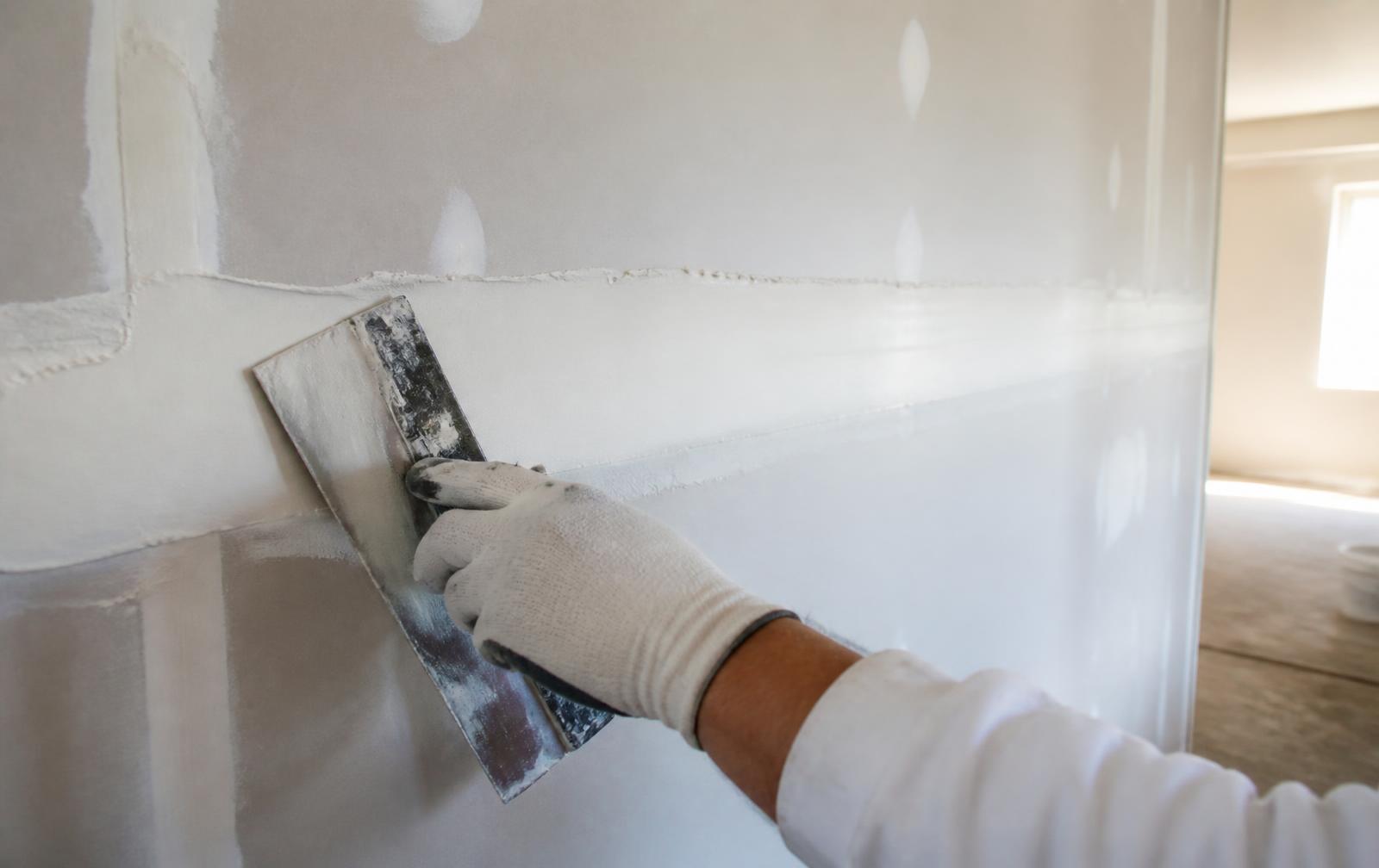 Finisher feathering joint compound across a drywall seam with a wide taping knife